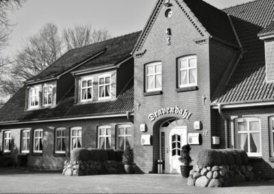 Die Schwarz-Weiß-Fotografie zeigt ein Ziegelgebäude. Über dem Eingang prangt die Schrift „Dravendahl“. Der Platz vor dem Haus ist gepflastert, auf der linken Seite des Gebäudes sind Bäume zu erkennen.